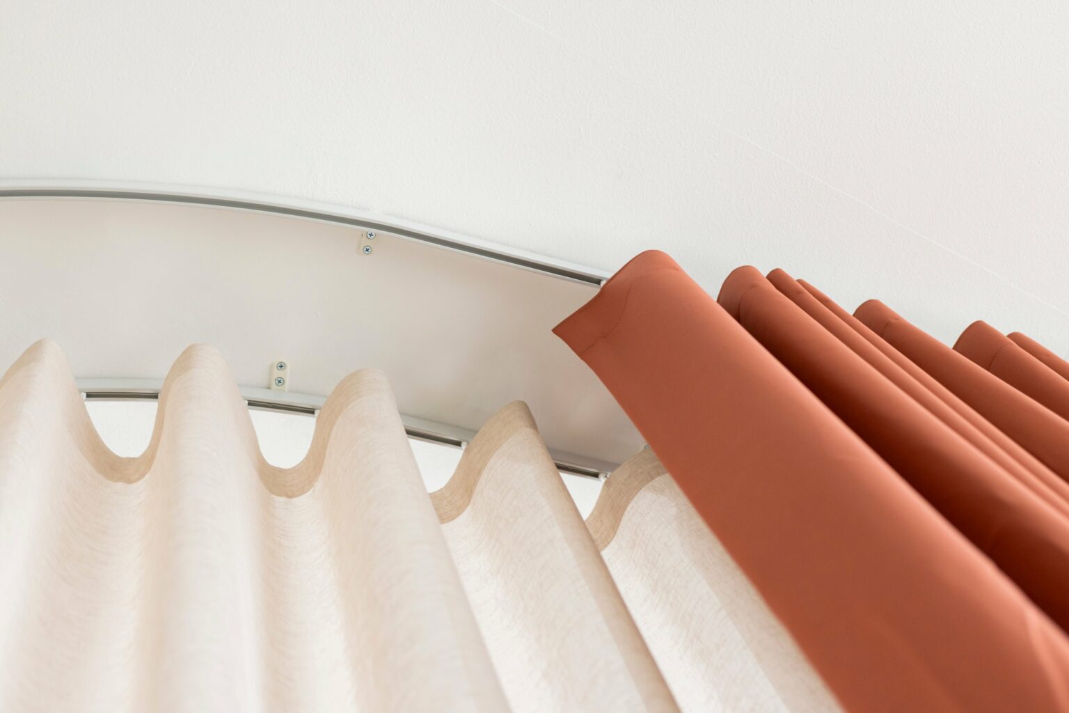Wave curtain heading on a bent ceiling-fixed curtain track, Proof FR sheer and Bossa FR solid