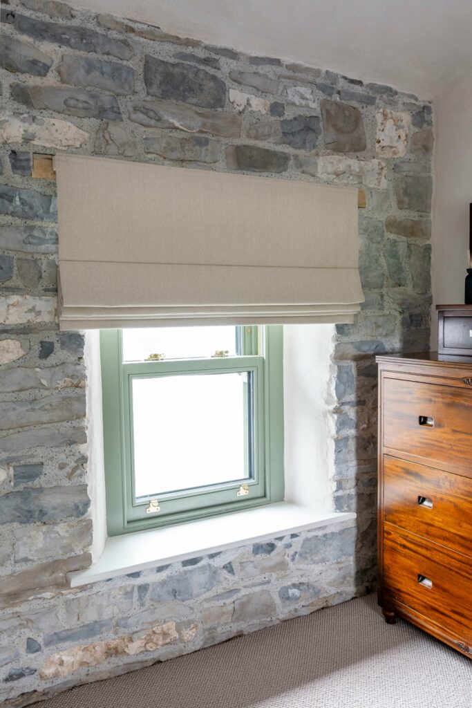 Made-to-measure Roman blind on an exposed stone wall above a sage green sash window, Midlands Gem