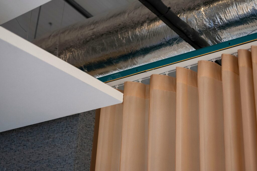 Wave curtain heading on a suspended track below exposed ductwork at PGIM Letterkenny